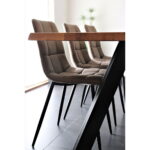 Vier Middelfart eetkamerstoelen in lichtbruin microvezel met zwarte poten (set van 2) staan langs één kant van een houten eettafel op een donkere vloer, met een potplant vaag op de achtergrond.