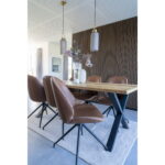 Een moderne eethoek heeft een houten tafel, drie sets Monte Carlo Dining Chairs with Swivel in vintage bruin PU en zwarte poten, hanglampen, decoratieve vazen met bloemen, een accentmuur van getextureerd hout en een neutraal vloerkleed onder de tafel.