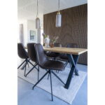 Een moderne eetkamer heeft een houten tafel, vijf Monaco Dining Chairs with Swivel in donkerbruin PU, zwarte metalen poten, twee hanglampen, een accentmuur met houten structuurpanelen, een lichtgrijs vloerkleed op tegelvloeren en vazen met bloemen op tafel.