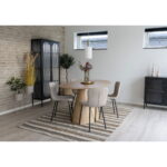 Moderne eetkamer met een ronde houten tafel, twee sets Halden eetkamerstoelen in beige bouclé met zwarte poten, een gestreept vloerkleed, planten, zwarte vitrinekast, minimalistische inrichting, lichte muren en grote ramen.