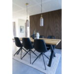 Moderne eetkamer met een houten tafel, een set van zes Monaco Dining Chairs with Swivel in zwart PU, lichtgrijs vloerkleed, twee hanglampen erboven, decoratieve vazen en planten op tafel en een houten accentmuur met latten op de achtergrond.