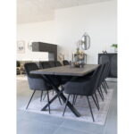 Een moderne eetkamer heeft een grote houten tafel en acht Harbo Dining Chairs van zwart fluweel met zwarte poten. Decoratieve items sieren de tafel, terwijl grijze tegelvloeren, neutrale muren en een minimalistische inrichting de ruimte compleet maken.