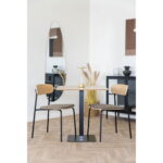 Een moderne eethoek met een vierkante houten tafel, een eetkamerstoel met essenhouten rugleuning, bruine zitting en zwarte poten (HN1269, set van 2), plus een gouden kandelaar, hoge spiegel, gedroogd gras in een vaas en minimalistisch decor tegen een witte muur.
