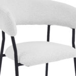 De Eetkamerstoel Ava - Bouclé Ivoor heeft een modern ontwerp met een gebogen, gestoffeerde rugleuning en zitting in ivoorkleurige bouclé stof, ondersteund door een zwart metalen frame en poten.