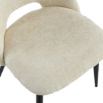 Close-up van Eetkamerstoel Monta - Beige, een moderne stoel met een gebogen rugleuning, beige bekleding en slanke zwarte poten.