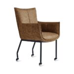 De Eetkamerstoel Thomas - Microleder Cognac is een bruin gestoffeerde fauteuil met een hoge rug, zwarte metalen poten en vier kleine wieltjes, schuin afgebeeld op een witte achtergrond.