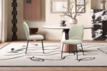 Moderne eetkamer met een ronde marmeren tafel, twee Stoel 'Lara' Stof Ote Sea 140 Ecru stoelen, een tapijt met abstract vispatroon, vaas met takken, ingelijste kunst op crèmekleurige muren en een open haard met een marmeren rand.