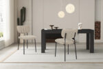Een moderne eetkamer met twee Stoel 'Antura' Stof Ote Lisa 170 Bruin stoelen en een zwarte tafel. Decoratieve items, een cactus, brandhout en ronde hanglampen versterken de minimalistische, neutraal getinte stijl van de kamer.