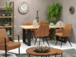 Een moderne eetkamer heeft een houten tafel met Eetkamerstoel Clark zwart Stof Soft Cognac stoelen, een wandklok, potplanten, decoratieve vazen, planken met ingelijste foto's op een grijze muur en een ronde salontafel met sierpompoenen.