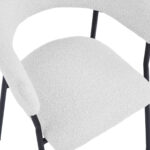 Een close-up van de Eetkamerstoel Ava - Bouclé Ivoor, met een gebogen, gestructureerde zitting en rugleuning van ivoorkleurige boucléstof op slanke zwarte metalen poten.