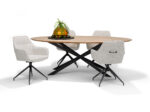 Een moderne ovale houten tafel met zwarte gekruiste poten wordt omringd door vier Toscane Eetkamerstoel - Stof Oasis Natural - draaivoet M4 draaistoelen, met een glazen schaal met een plant als middelpunt.