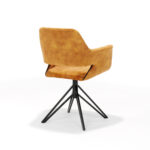 De Katy Eetkamerstoel - Aurora Velours Gold is een moderne fauteuil met goudkleurige velours bekleding, een schuine rugleuning en zwarte geometrische metalen poten met een draaivoet, afgebeeld op een witte achtergrond.