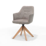 De Calvin Eetkamerstoel draaivoet Eiken Stof Soft Pebble is een moderne fauteuil met lichtgrijze bekleding, gecapitonneerde zitting en rugleuning, vier schuine eikenhouten poten en een draaivoet. Eigentijds ontwerp gefotografeerd tegen een witte achtergrond.