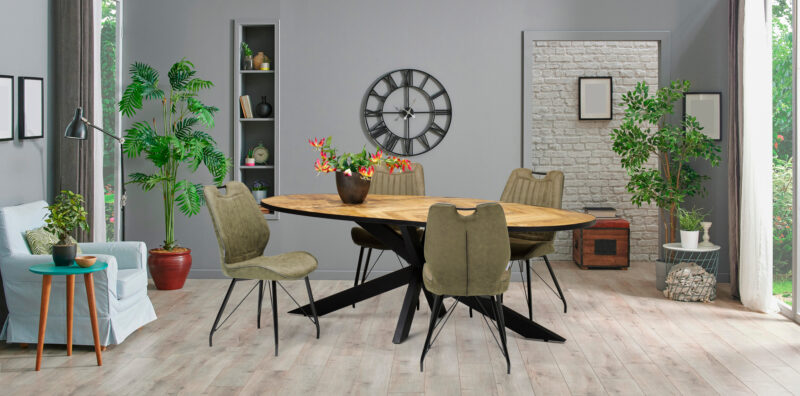 Moderne eetkamer met een ovale houten tafel, vijf Stoel Penta zwart stof Soft Groen stoelen, planten, wandklok, boekenplank en grote ramen voor natuurlijk licht. Een lichte houten vloer en neutrale muren geven de kamer een gezellige uitstraling.