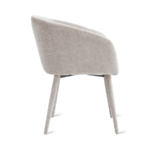 De Eetkamerstoel Nova - Beige is een moderne, lichtbeige gestoffeerde stoel met vier taps toelopende poten en een gebogen rugleuning, van opzij gezien tegen een witte achtergrond. Het minimalistische ontwerp voegt elegantie toe aan elke ruimte.
