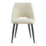 De Eetkamerstoel Monta - Beige is een moderne stoel met een beige gestoffeerde zitting en rugleuning, slanke zwarte metalen poten en een subtiele opening tussen de zitting en rugleuning voor extra stijl.