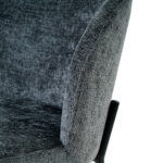 Close-up van Eetkamerstoel Lio - Antraciet, met donkergrijze bekleding met zichtbare rugleuning, armleuning, deel van de zitting en een zwart metalen frame rechts.