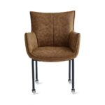 De Eetkamerstoel Thomas - Microleder Cognac is een bruin gestoffeerde fauteuil met een gebogen rugleuning, armleuningen en vier zwart metalen poten met wieltjes, afgebeeld tegen een effen witte achtergrond.