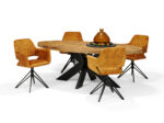 Een houten ovale eettafel met een zwart geometrisch metalen onderstel, omringd door vier Katy Eetkamerstoel - Aurora Velours Hunter stoelen met een draaibaar onderstel. De tafel heeft een decoratief middenstuk met een bruine fles en kleine ronde objecten.