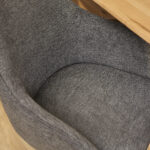Close-up van de Eetkamerstoel Jens Antraciet, een moderne grijze stoffen stoel met een gebogen zitting en rugleuning, getoond naast een lichthouten tafel.