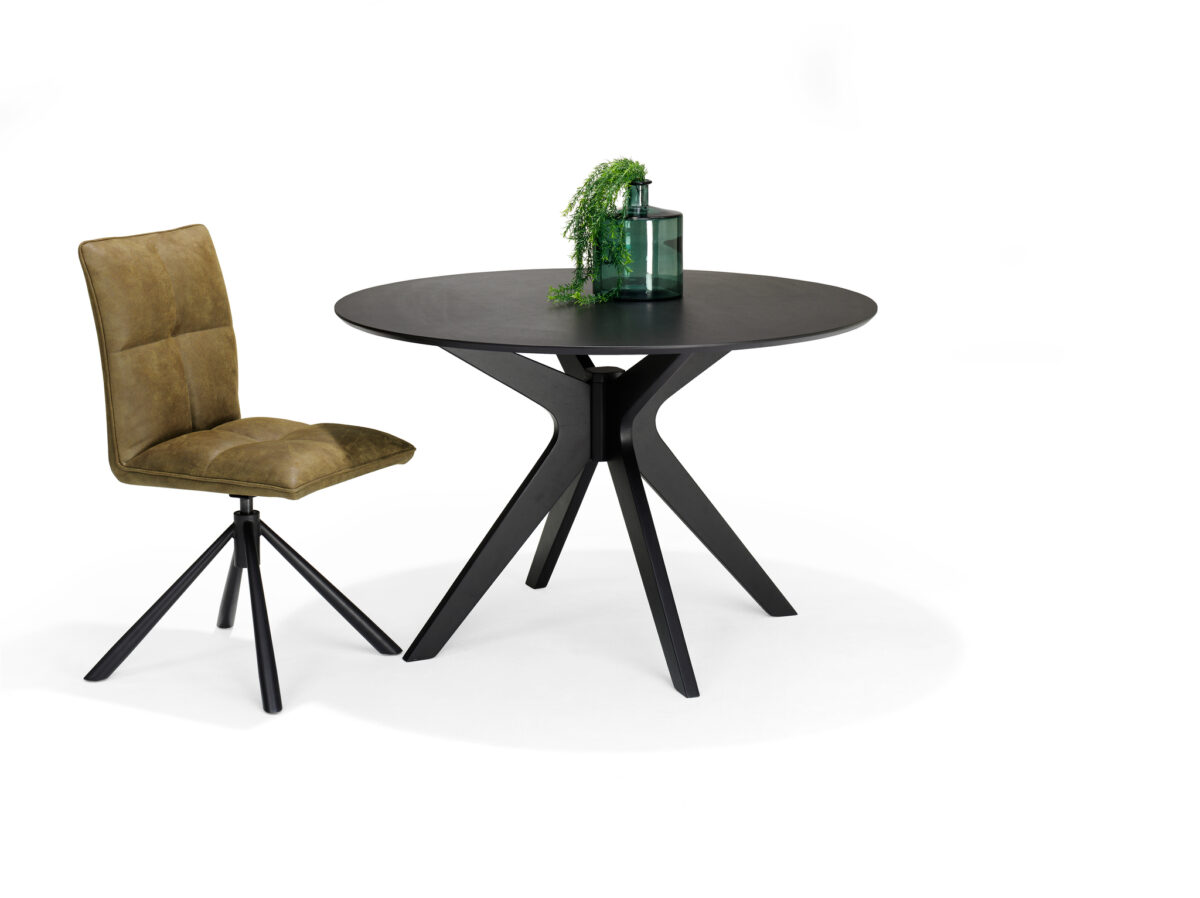Een ronde zwarte tafel met een modern driepootonderstel staat op een witte achtergrond. Erbij staat een olijfgroene stoel met metalen onderstel. Een groene plant in een doorzichtige fles siert de tafel.