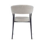 De Eetkamerstoel Ava - Bouclé Taupe is een moderne stoel met een gebogen, gestoffeerde taupe rugleuning en zitting, ondersteund door slanke zwart metalen poten, te zien vanaf de achterkant.