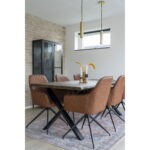 Een moderne eetkamer met een houten tafel, zes Harbo Dining Chairs met draaibare zitting in vintage bruin PU en zwarte poten (HN1220), een vloerkleed met patroon, een glazen kast, twee gouden hanglampen en vazen met droogbloemen op tafel. Natuurlijk licht stroomt door een klein raam.
