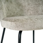 Close-up van de Eetkamerstoel Lio - Naturel, met een lichtbeige gestructureerde stoffen zitting en rugleuning en slanke zwarte metalen poten.