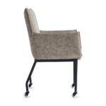 De Eetkamerstoel Thomas - Microleder Taupe is een moderne stoel met een hoge rugleuning, armleuningen, lichtbruine microlederen bekleding, zwarte metalen poten en vier wielen voor eenvoudige verplaatsing. De afbeelding toont het zijaanzicht van de stoel.