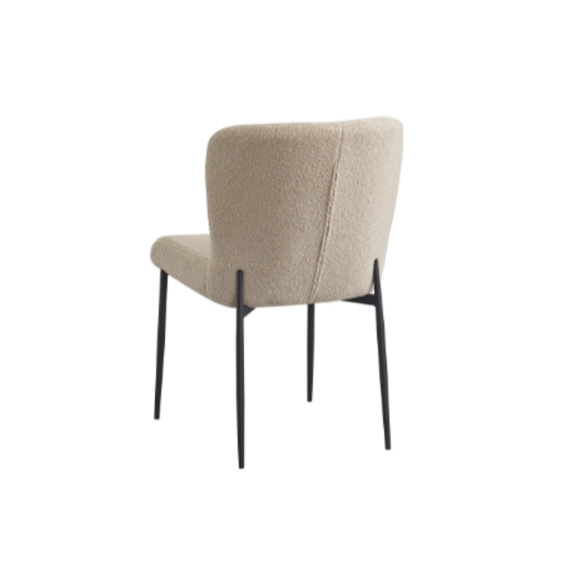 De Eetkamerstoel Tess Beige is een moderne stoel met een beige gestoffeerde zitting en rugleuning, slanke zwarte metalen poten, getoond vanuit een hoek op de achterkant tegen een witte achtergrond.