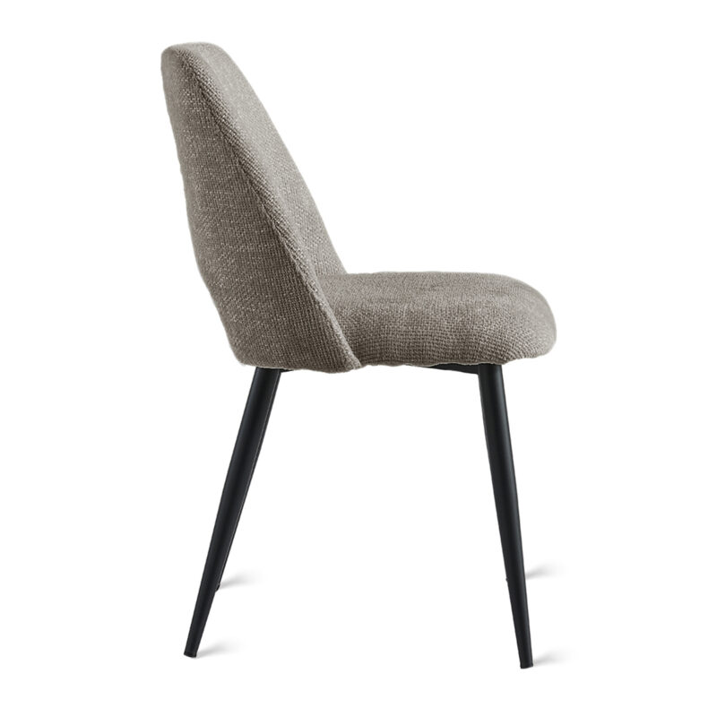 De Eetkamerstoel Monta - Taupe is een moderne stoel met een beige gestoffeerde zitting en rugleuning, slanke zwarte metalen poten, afgebeeld in zijaanzicht tegen een witte achtergrond.