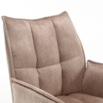 Close-up van de Eetkamerstoel Dani, een moderne fauteuil met hoge rugleuning bekleed met zacht fluweelbeige stof met zichtbaar doorgestikt stiksel op de rugleuning en zijkanten, tegen een effen witte achtergrond.