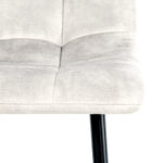 Close-up van de lichtgrijze zitting van Eetkamerstoel Yerevan Velvet Taupe met zichtbare stiksels en een zwarte metalen poot tegen een witte achtergrond.