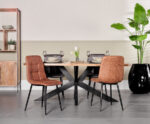 Een moderne eetkamer met een houten tafel, zwarte metalen poten, twee Eetkamerstoel Yerevan Cognac stoelen, twee grijze stoelen met kussens, servies voor vier personen, een grote potplant en een houten kast tegen een beige muur.