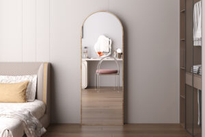 De Spiegel 'Rosalie' 160x60 Oude eik (1c), een hoge gewelfde spiegel, staat tegen een grijze muur en weerspiegelt een badmeubel met een ronde spiegel en een stoel met roze kussens, terwijl aan weerszijden delen van het bed en de open kast zichtbaar zijn.