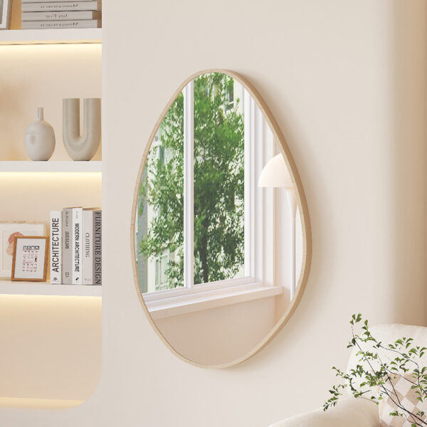 Een moderne, minimalistische woonkamer heeft ingebouwde planken met decoratieve vazen, de 'Rana' 80x50 Oude eik spiegel die een raam met groen weerspiegelt, een sofa met een kussen met patroon en een bladplant in de buurt.