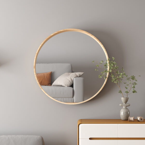 De 'Ria' 80x80 oude eik spiegel weerspiegelt een bank met kussens; onder een dressoir staat een vaas met groene takken, ingelijste kunst en boeken op een zwevende plank tegen een lichtgrijze muur.