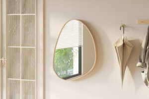 Een beige kamer is voorzien van de Spiegel 'Roza' 80x60 Oude eik (1c), een ronde asymmetrische spiegel die een raam met jaloezieën en groene bomen weerspiegelt, met een beige paraplu en jas die aan een houten rek vlakbij hangen.