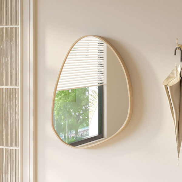 Een beige kamer is voorzien van de Spiegel 'Roza' 80x60 Oude eik (1c), een ronde asymmetrische spiegel die een raam met jaloezieën en groene bomen weerspiegelt, met een beige paraplu en jas die aan een houten rek vlakbij hangen.