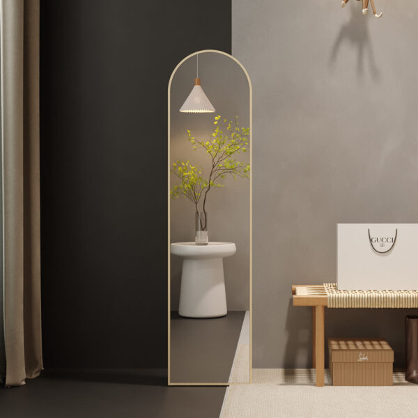 Een moderne minimalistische entree heeft de hoge Spiegel 'Rosalie' 160x40 Oude eik (1c) boogspiegel, een witte kruk met groene takken in een vaas, een geweven bank, neutrale muurkunst, bruine kussens en een Gucci boodschappentas op de vloer.