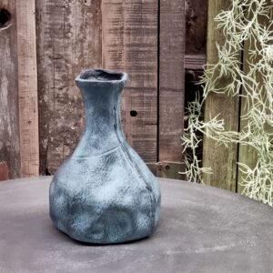 Een set van 4 Vaasje Blauw Gemeleerd, met blauw gestructureerd keramiek met een onregelmatige vorm, staat op een grijs oppervlak tegen rustieke houten planken en hangend groen.