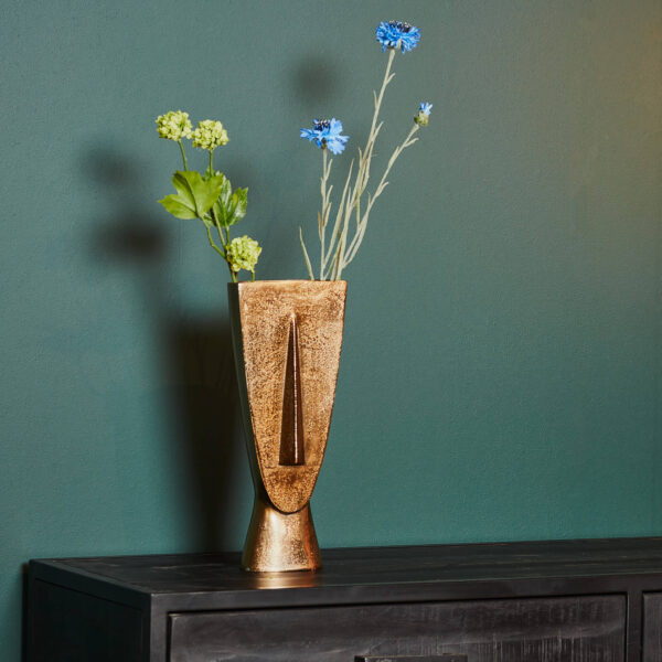 De Vaas Fin - Antiek goud | Small staat op een donkere houten kast tegen een donkergroene muur, gevuld met groene en blauwe bloemen.