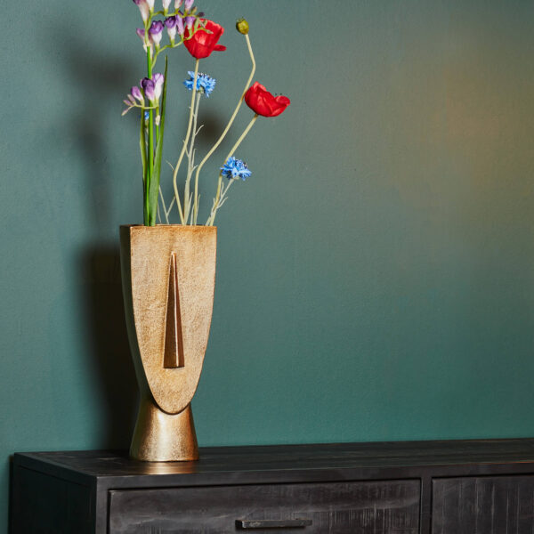 De Vaas Fin - Antiek goud | Large, gevuld met rode, paarse en blauwe kunstbloemen, staat op een donkere houten kast tegen een effen groene muur.