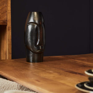 De Vaas Lyra - Zwart | Small, een zwarte abstracte vaas in de vorm van een gezicht, staat op een houten tafel met een deel van een houten kast en een donkere muur op de achtergrond.
