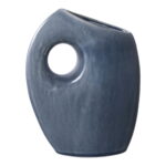 Een moderne vaas van blauw keramiek met een asymmetrische vorm, een groot rond gat bij de bovenkant en een licht ongelijkmatige, glanzende afwerking.