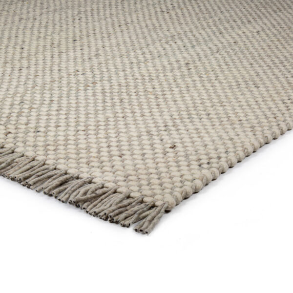 Een close-up van de hoek van het Burano White Grey 001-367 170x230 tapijt, met een lichtbeige grof geweven textuur en korte franjes langs de rand, op een wit oppervlak.