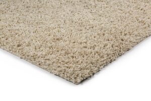 Close-up van de hoek van het Berbero Lungo Cloud White 815 200x300 tapijt, met dikke, beige shaggy vezels op een witte achtergrond.