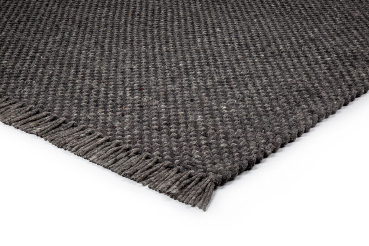 Een close-up van het Burano Anthracite 614-604 170x230 tapijt met donkergrijze structuur en franje, tegen een witte achtergrond.