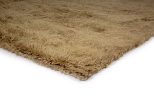 Close-up van de hoek van het Merano Beige 002 200x300 tapijt, met de pluizige, dikke, lichtbruine shagtextuur en licht ongelijkmatige pool tegen een witte achtergrond.