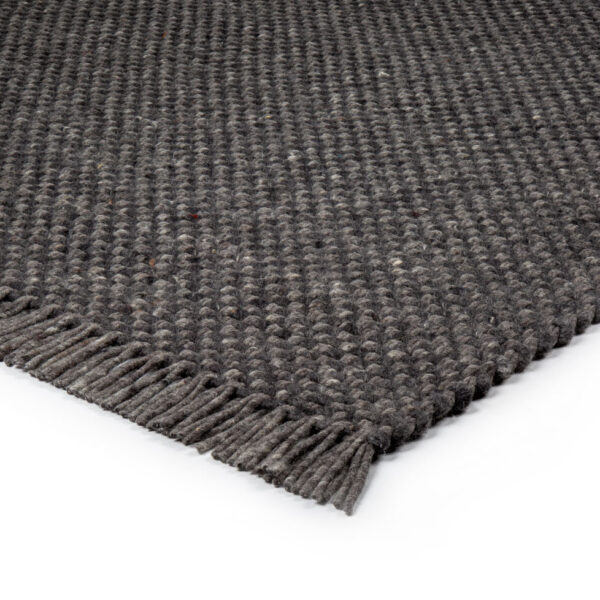 Een close-up van het Burano Anthracite 614-604 200x300 tapijt toont de donkergrijze geweven textuur met een uniek patroon en korte franjes langs de rand, tegen een witte achtergrond.